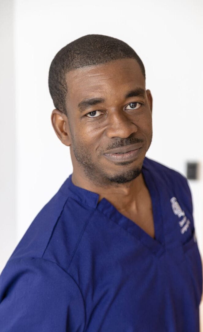 Man wearing blue medical scrubs, smiling.