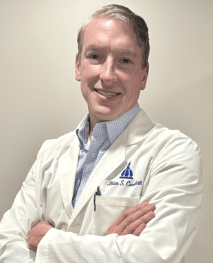 Smiling doctor in white coat, arms crossed.